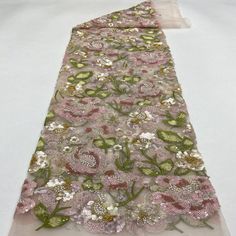 a pink and green flowered lace with sequins on the edge is laying on a white surface