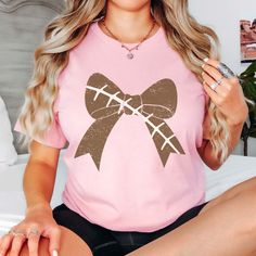 Score a touchdown with our Football Large Bow Bella Tee! Gear up for game day in style with our Football Large Bow Bella Tee, the perfect blend of sporty chic and feminine flair. Crafted from premium, ultra-soft fabric, this tee is as comfortable as it is stylish, making it the ideal choice for cheering on your favorite team from the stands or enjoying a casual day out with friends. The standout feature? A large bow, right on trend with football stitching, adding a touch of playful charm to the classic football-inspired design. But it's not just about looks – our Bella Tee is designed with your comfort in mind, so you can focus on the game without any distractions. The relaxed fit and breathable fabric keep you cool and comfortable, inning after inning. Available in a range of colors, our Pink Sporty T-shirt For Fall, Football Season Team Spirit T-shirt, Sporty Pink Tops For Game Day, Cheerleading Tops For Fall, Pink Game Day Top With Team Spirit, Pink Team Spirit Tops For Game Day, Team Spirit Pink Tops For Game Day, Pink Team Spirit Game Day Top, Pink Tops For Game Day With Team Spirit Style