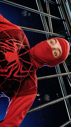 a man wearing a red hoodie standing in front of a metal wire fence and looking up at the camera