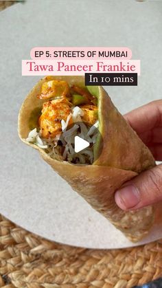 a hand holding a wrap filled with food on top of a white plate next to a woven place mat