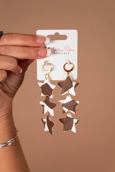 a person holding up two pairs of star shaped earrings in front of a brown and white background