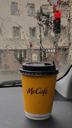 a yellow coffee cup sitting on top of a table next to a window with the words mccaf written on it