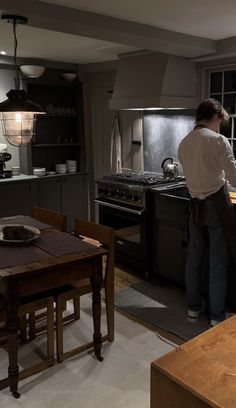 a woman standing in a kitchen next to a stove top oven and table with chairs