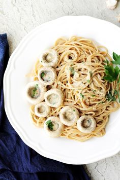 a white plate topped with pasta covered in mushrooms and parsley next to a blue napkin