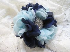 a blue and white flower brooch on top of a lace covered fabric bed sheet