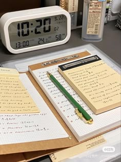 an alarm clock sitting on top of a desk next to notebooks and papers in front of it