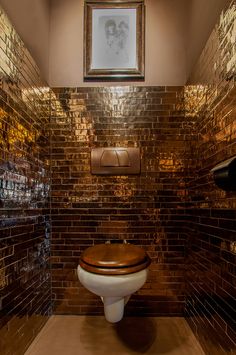 a toilet in a bathroom with brown and gold tiles on the walls, along with a wooden seat