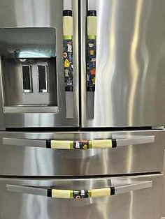 two stainless steel refrigerators with yellow handles and tags on the doors, in a kitchen