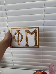 a person holding up a piece of paper with the letter m in gold on it