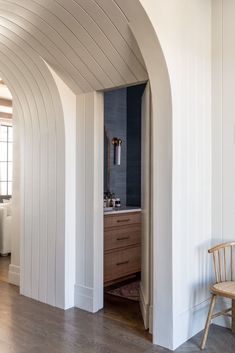 an arched doorway leads to a bathroom with wood floors and white walls, along with a wooden chair