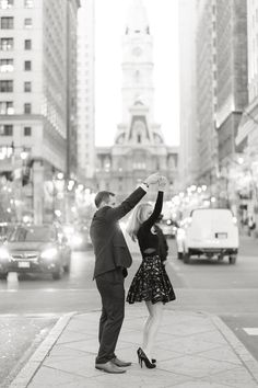 a man and woman dancing on the sidewalk in front of tall buildings with cars behind them