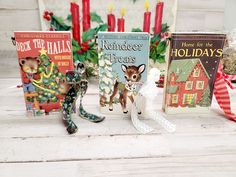 three christmas books are sitting next to each other on a white wooden table with candles in the background