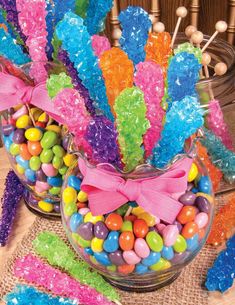 colorful candies are in a glass bowl on a table next to candy sticks and lollipops