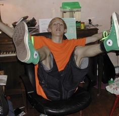 a young man sitting in an office chair with his feet up on the computer desk