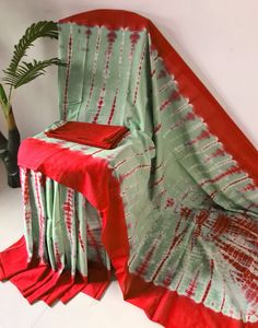 a red and green tie - dyed table cloth on a chair with a plant in the corner