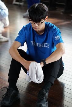 a young man sitting on the floor with his hands in his pockets and looking down