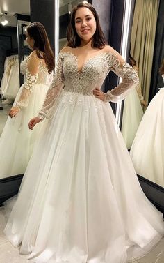 a woman standing in front of a mirror wearing a wedding dress with long sleeves and lace