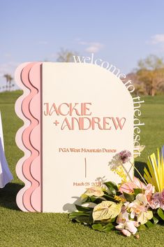 a welcome sign with flowers on the grass in front of it at a wedding ceremony