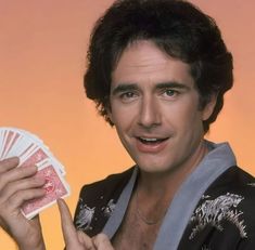 a man holding four cards in one hand and smiling at the camera while wearing a kimono