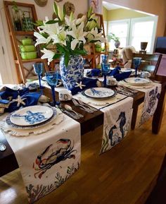 a dining room table set with blue and white plates, napkins, and flowers