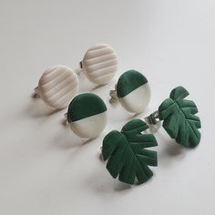 four pairs of earrings with green and white leaves on them, sitting on a table