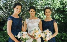 three beautiful women standing next to each other in front of some trees and bushes holding bouquets