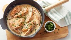 a pan filled with chicken and sauce on top of a wooden cutting board