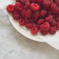 fresh raspberries on a white plate sitting on a marble table