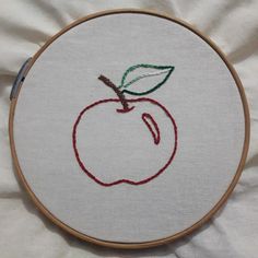 an embroidered apple with a green leaf on it is sitting on a white sheet in front of a wooden hoop