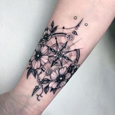 a black and white photo of a tattoo with flowers on the arm, which has a compass in it