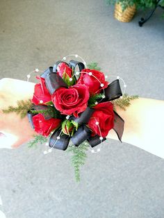 a woman's hand holding a bouquet of red roses and greenery in it