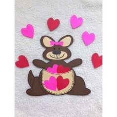 a teddy bear holding a heart in its pocket with hearts flying around it on a white towel