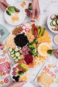 several people are holding their hands over a large platter of food that includes cucumbers, celery, broccoli and crackers