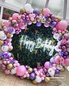 a happy birthday sign surrounded by balloons and greenery in the shape of a circle