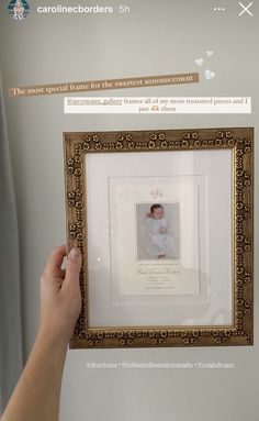 a person holding up a frame with a baby's picture on it in front of a window