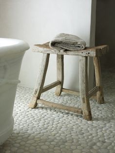 an old wooden stool sitting next to a bath tub in a bathroom with white walls