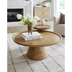 a living room with a coffee table and white flowers on the end tables in front of a fireplace