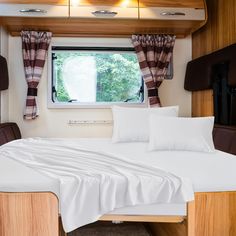 a bed with white sheets and pillows next to a window in a room that has wood trim