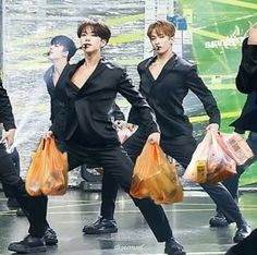 group of men in black suits carrying bags on stage with one man holding an orange bag