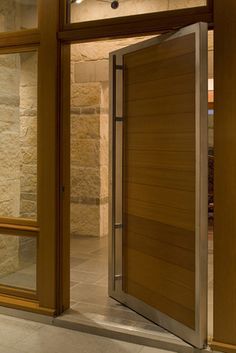 an open wooden door in front of a stone building with glass walls and doors on both sides