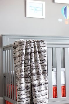 a baby crib with an orange and white blanket on the bottom, next to a hot air balloon