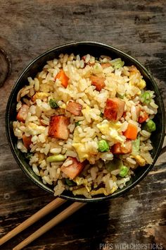 a bowl filled with rice and vegetables next to chopsticks on a wooden table