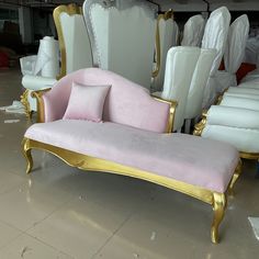 a pink and gold chaise lounge in a room filled with white chairs, pillows and other furniture