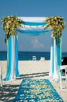 an outdoor ceremony setup on the beach with blue and white draping, flowers and chairs