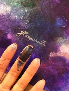 a woman's hand with nail polish on top of a purple and blue painting