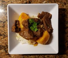 a white plate topped with meat, rice and oranges on top of a counter