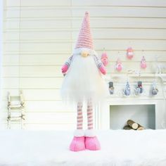 a white and pink gnome doll sitting on top of a bed next to a fireplace