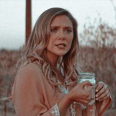 a woman holding a mason jar in her right hand and looking off to the side