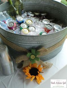 a bucket filled with bottles and cans sitting on top of a table next to a sunflower