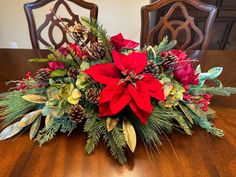 a christmas centerpiece with poinsettia, pine cones and greenery on a wooden table